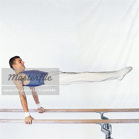 Jeune gymnaste masculin effectuant de routine sur les barres parallèles, vue latérale