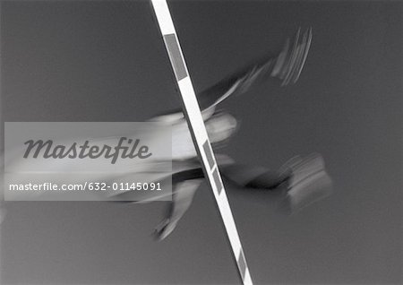 Male athlete jumping hurdle, low angle view, blurred motion, b&w