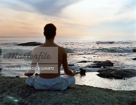 Homme assis en position du lotus en face de la mer, vue arrière, silhouette