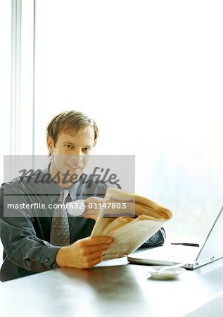 Businessman sitting at desk, drinking and reading