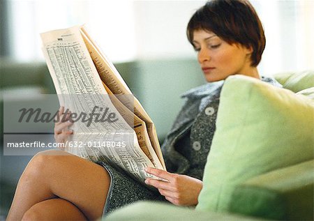 Femme assise avec les jambes croisées, lisant journal d'affaires