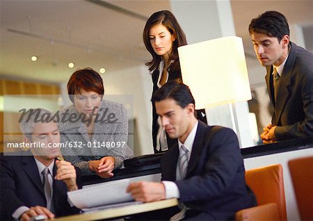 Group of business people, standing and sitting, looking at document, tilt