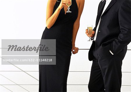 Well-dressed couple standing together drinking champagne, mid-section