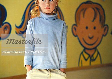 Little girl standing with hands in pockets, looking away, mural in background