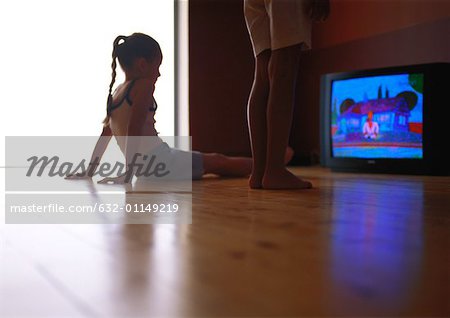 Kleines Mädchen auf Boden beobachten Televison, zweite Person steht neben ihr sitzend