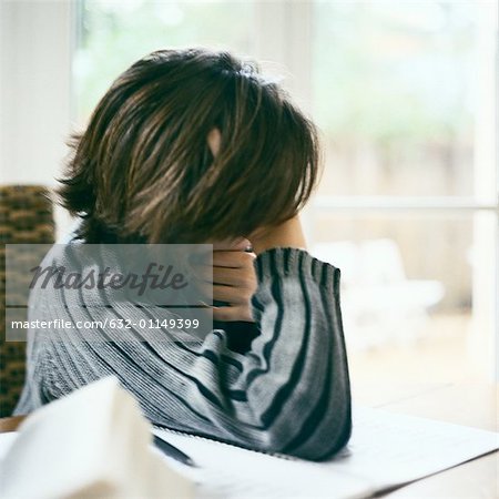 Child leaning on table, looking out window, distracted from doing homework