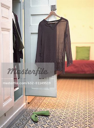 Open closet with blouse hanging from door and pair of shoes on floor
