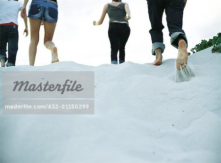 Four people running on sand, low section, rear view