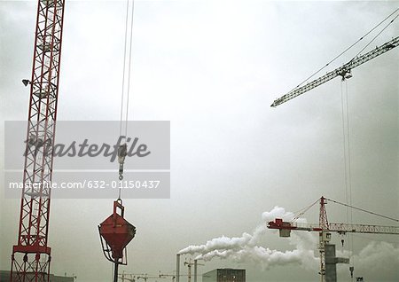 Cranes and factory smoke stacks, low angle view