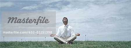 Man in business clothes sitting in lotus position on grass with head back and eyes closed, front view