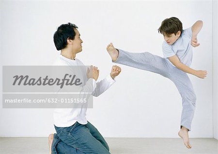 Boy giving karate kick in mid air, man on knees with fists out