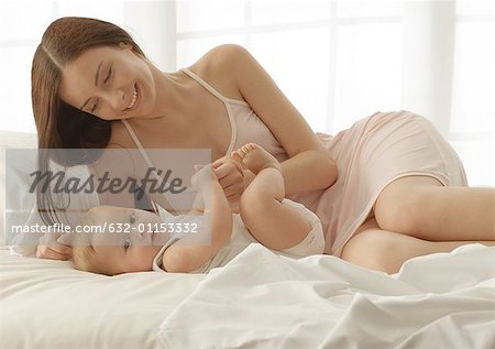 Mother and baby lying on bed, baby looking at camera