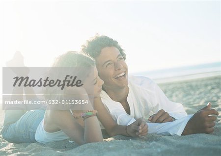 Teenage couple lying on stomachs on beach, talking