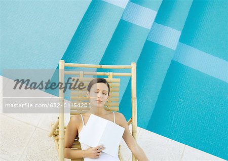 Femme allongée dans une chaise longue au bord de la piscine avec le livre sur la poitrine