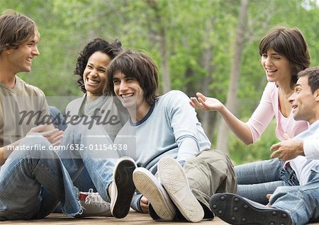 Group of young friends sitting around together outdoors, laughing