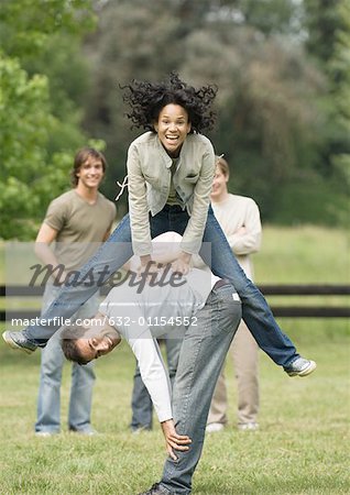 Young woman playing leapfrog with young man while friends look on