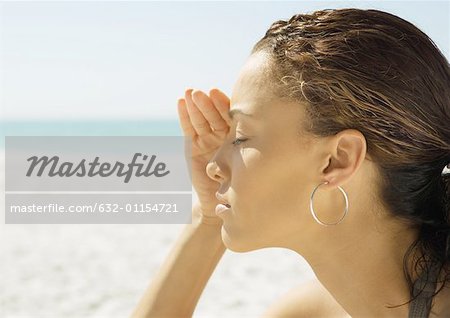 Woman shading eyes on beach, close-up