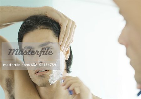 Man shaving cheek in mirror