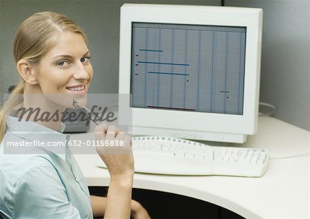 Female office worker sitting at computer, smiling at camera
