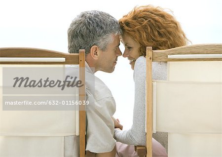 Couple d'âge mûr assis dans des chaises de plage, toucher le front