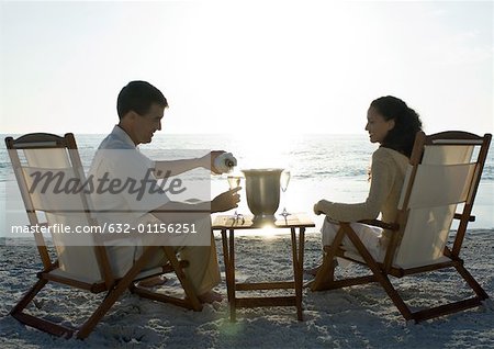 Newlyweds, husband serving wife champagne on beach
