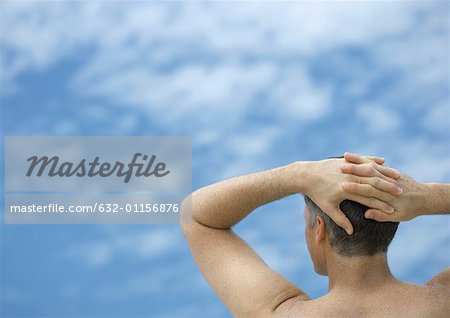 Man with hands behind head, looking at sky, rear view