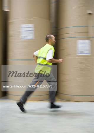 Man running past rolls of paper in warehouse