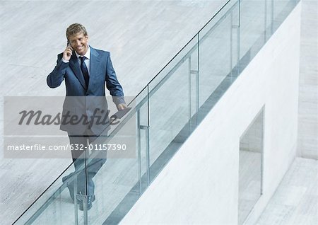 Businessman leaning on railing, using cell phone, high angle view