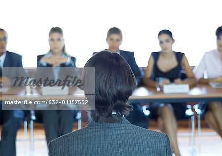 Executives sitting at conference table, looking at man in foreground