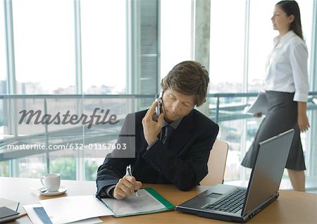Homme d'affaires en utilisant le téléphone cellulaire au bureau pendant que le travailleur d'employées de bureau passe en arrière-plan