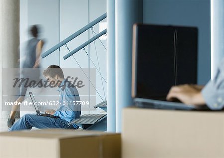 Homme d'affaires utilisant un ordinateur portable, la seconde personne utilise l'ordinateur portable sur une boîte en carton en avant-plan flou