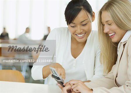 Two young business women looking at cell phone together