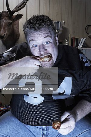 Man Watching Television and Eating Chicken Wings