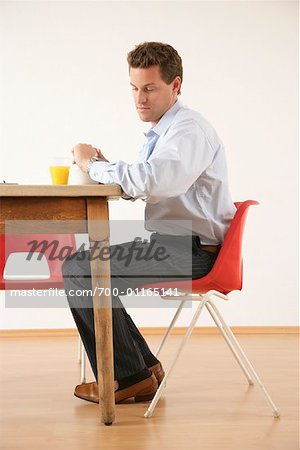 Man Looking at Wristwatch at Breakfast Table