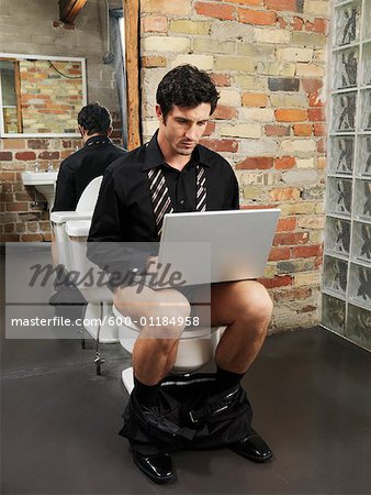 Mann sitzt auf Toilette mit Laptopcomputer