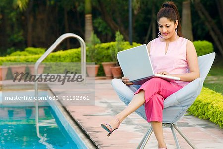 Junge Frau mit einem Laptop am Pool