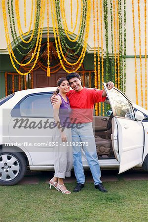 Portrait of a young couple standing near the open door of a car and smiling