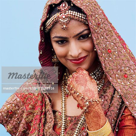 Portrait of a bride in a traditional wedding dress smiling with her hand on her chin