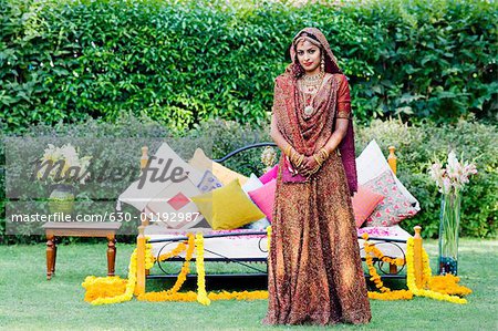 Portrait of a bride in a traditional wedding dress standing in front of a bed on the lawn