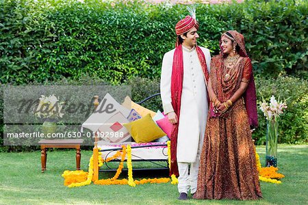 Newlywed couple in traditional wedding dress standing in front of a bed in a lawn