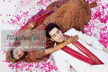 High angle view of a newlywed couple in traditional wedding outfits sleeping on the bed