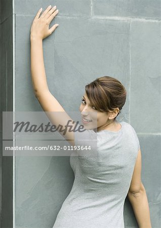 Woman leaning against wall, looking over shoulder at camera, portrait