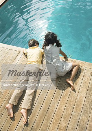 Boy and girl sitting at edge of swimming pool, high angle view