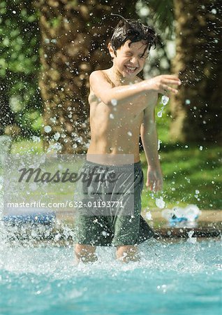 Boy standing in swimming pool, splashing