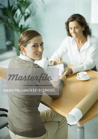 Woman sitting at table across from architect, smiling over shoulder at camera