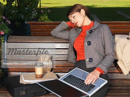 Femme s'endormir sur le banc de parc, tout en utilisant l'ordinateur portable