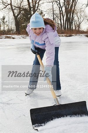 Fille pelleter de la neige de la patinoire