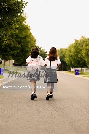Vue arrière de deux écolières de marcher sur la route