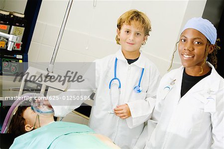 Boy imitating a doctor and adjusting the oxygen mask of a patient with a female doctor standing beside him