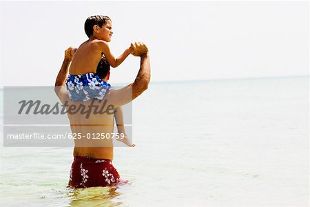 Vue arrière d'un homme adult moyen portant son fils sur ses épaules sur la plage